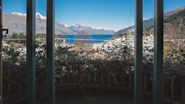 Vista desde un balcón cubierto con columnas, sobre un lago, montañas y un pueblo.