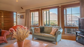 Un salón espacioso con un amplio ventanal que ofrece vistas a la montaña, una mesa de madera, un sofá azul y un sillón rojo.