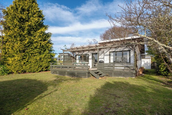 A cabin with a wooden deck, a covered porch, and a large evergreen tree in the background.