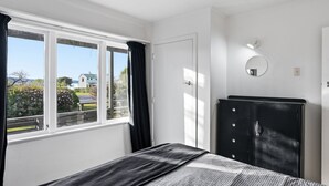 Un dormitorio con cama, armario, ventana con cortinas y una lámpara fijada a la pared.
