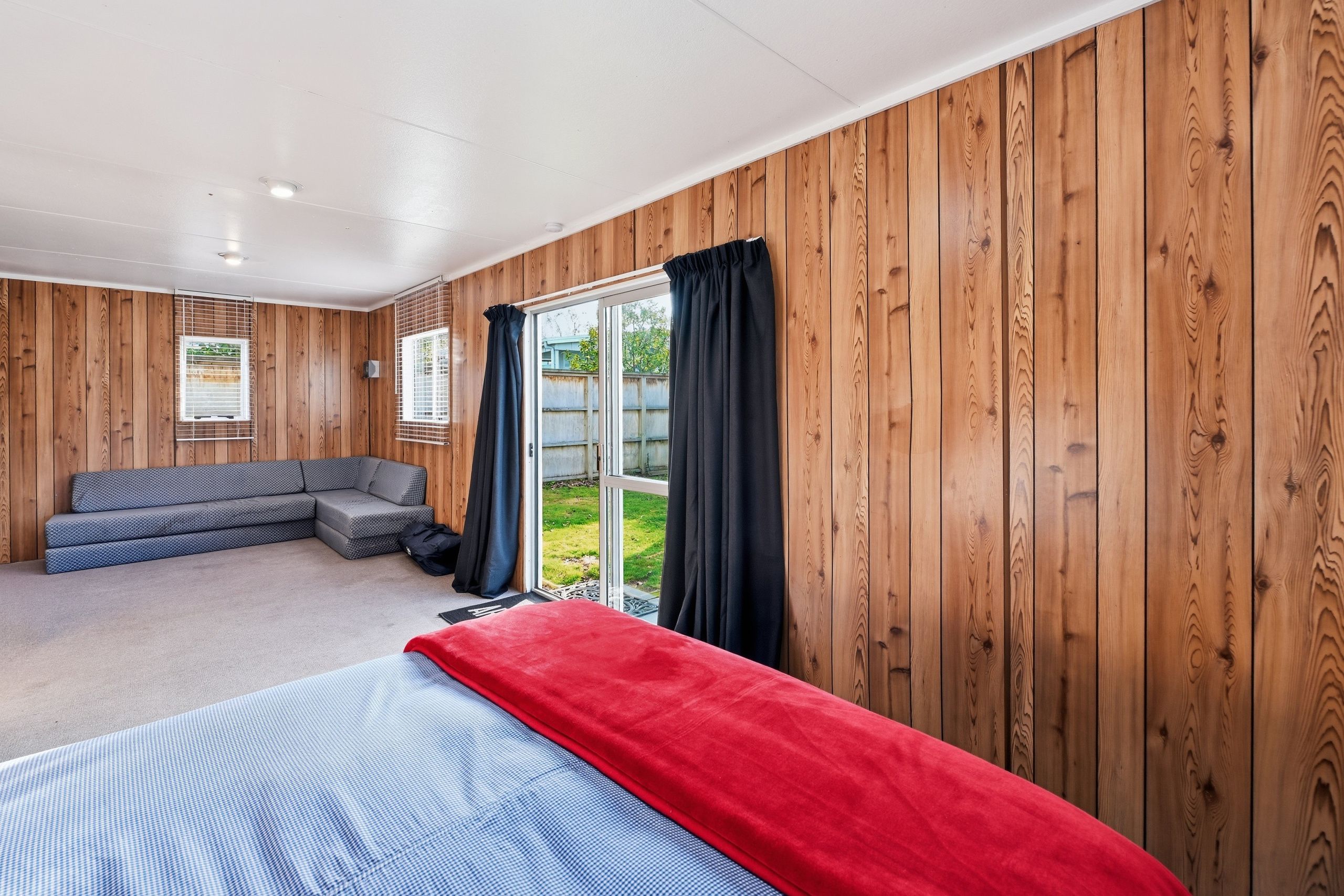 A room with a bed, a sofa, and a sliding glass door leading to a garden.