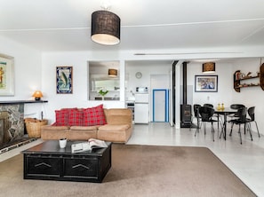A modern living room with a sofa, coffee table, and fireplace. There is a kitchen area with a stove and dining table with chairs. - Wharewaka Bach - Lake Taupo Holiday Home (Wharewaka)