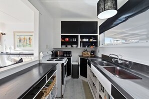 Una cocina moderna con encimera negra, armarios blancos y un amplio ventanal.