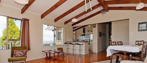 Amplia sala de estar con techo alto, vigas de madera, una mesa de comedor y una cocina al fondo.