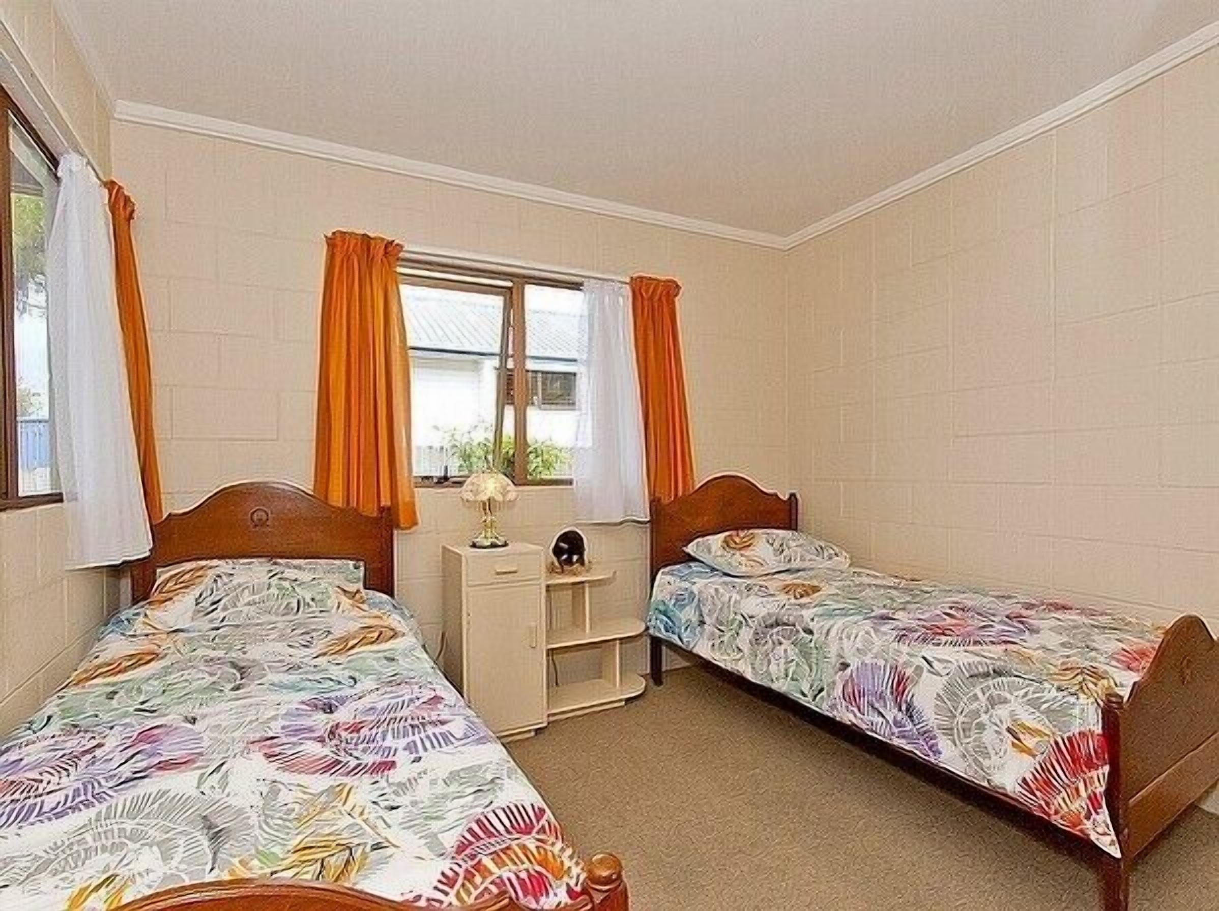 A bedroom with two single beds, a nightstand, a lamp, and a window with curtains.