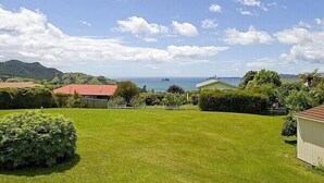 A grassy area with a building and a view of the sea. - Views on Rimu - Whitianga Holiday Home (Whitianga)