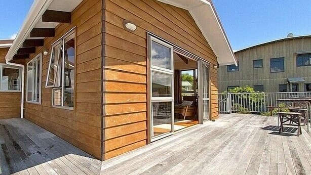 A wooden cabin with a deck, large windows, and a door leading to an interior space. - Views on Rimu - Whitianga Holiday Home (Whitianga)