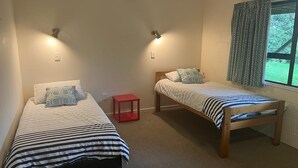 A bedroom with two single beds, a red stool, and a window with curtains. - Aqua Views - Kuratau Holiday Home (Kuratau)