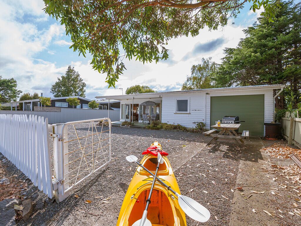 A kayak with paddles in a gravel area with a white fence and a green garage in the background.