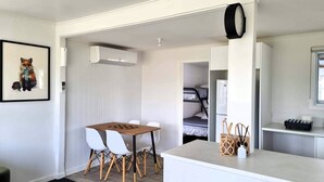 A compact room with a dining table, chairs, a small kitchen area, and a bunk bed in the background. - The reviews say it all! A blissful bach, & pet friendly! (Mangakino)