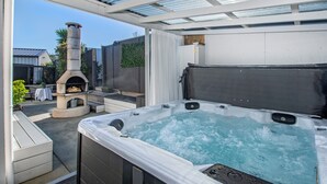 A hot tub with a stone fireplace and a pergola overhead.