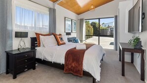 A bedroom with a large bed, a nightstand, a bedside table, a TV, and a view of the outside.