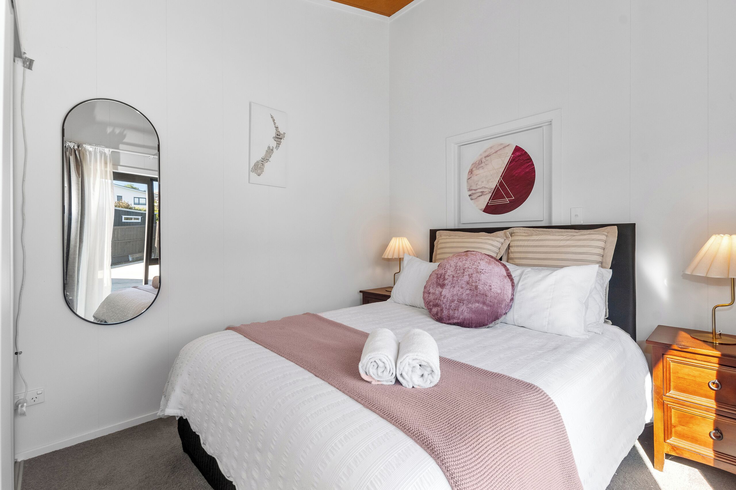 Een net opgemaakt bed met een roze deken, twee kussens en twee opgerolde handdoeken.