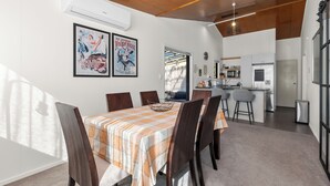 A dining area with a table set for six, a kitchen in the background, and a ceiling with wooden beams.