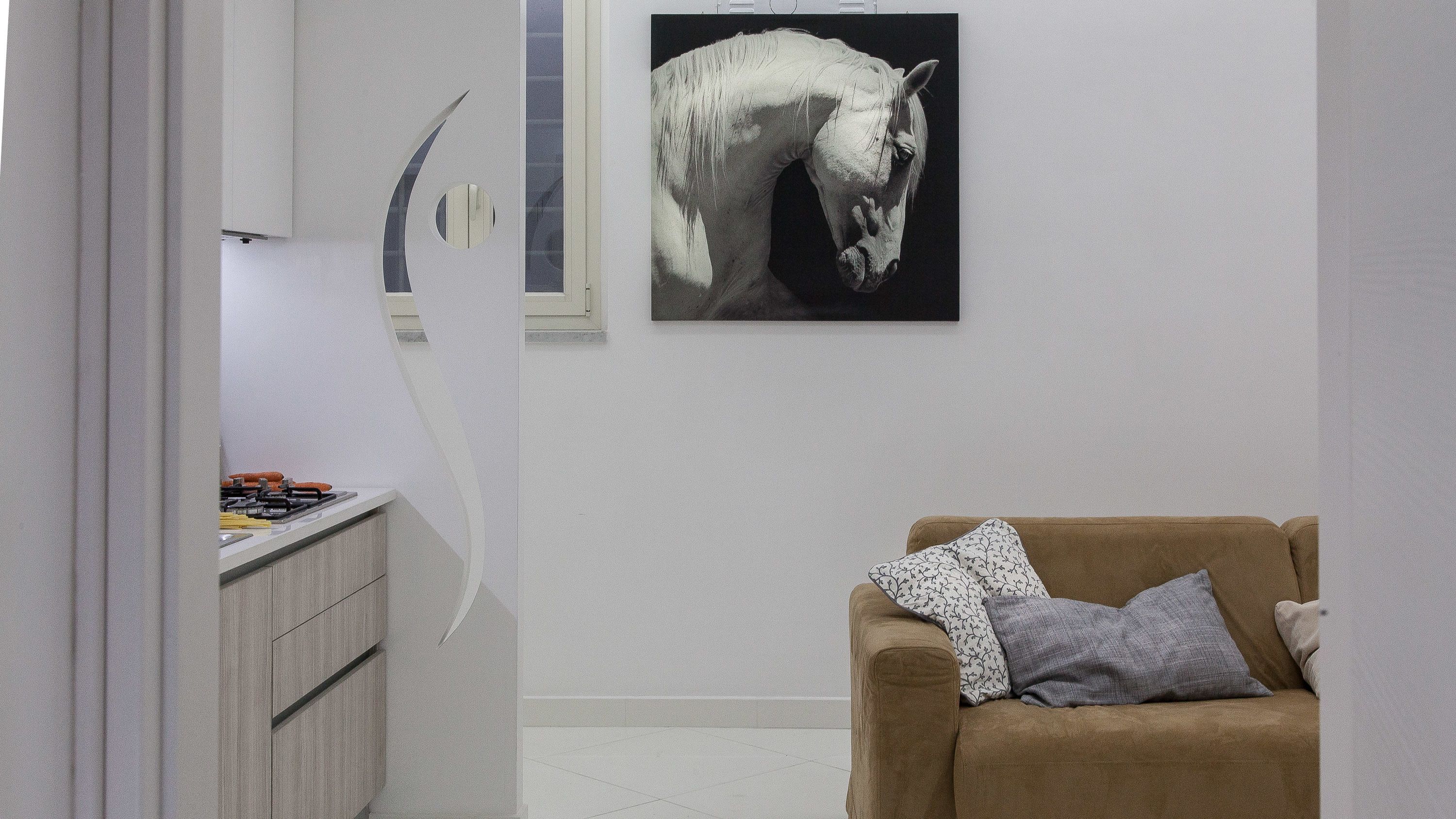 Een moderne kamer met een minimalistisch design, met een bruine bank met gestreepte kussens, een witte kast met gereedschap, en een zwart-wit paardenschilderij aan de muur.