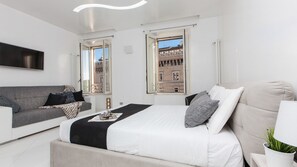 Ein modernes Schlafzimmer mit einem Bett, zwei Sofas, einem Fernseher und großen Fenstern mit Blick auf die Stadt.