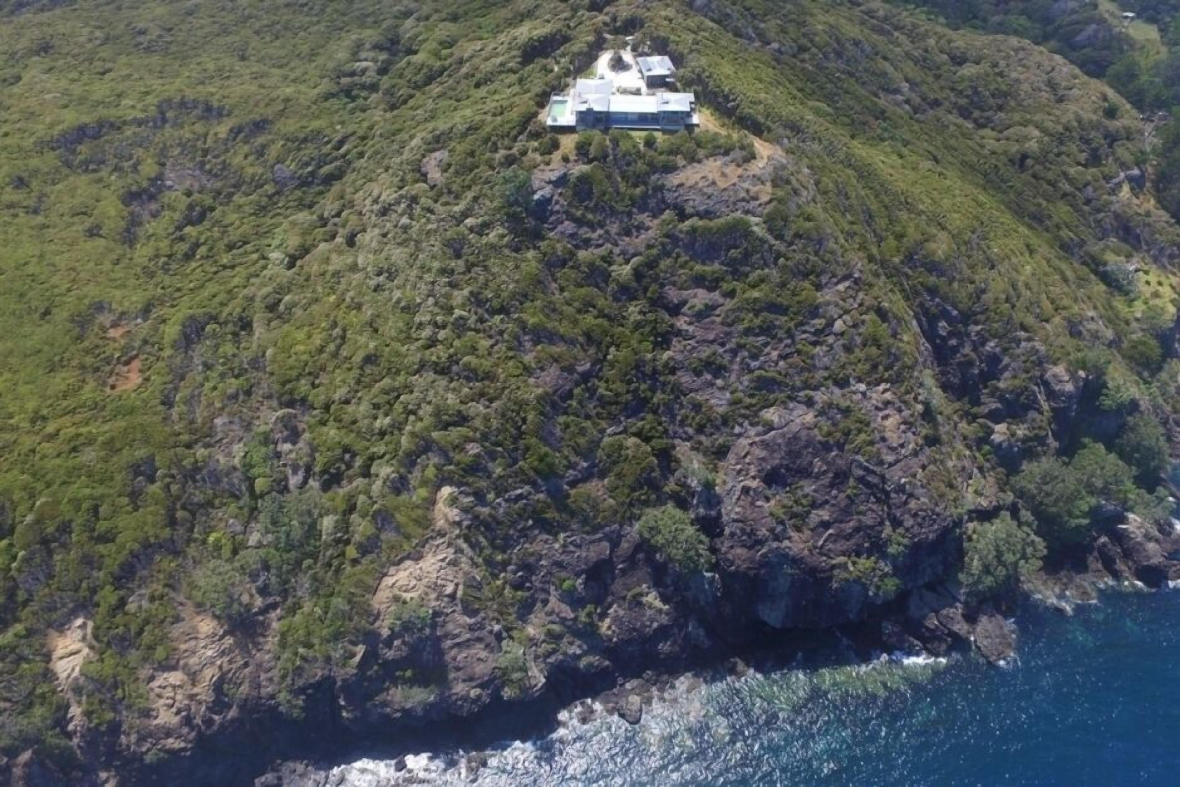 A coastal property with a prominent building on a hill, surrounded by dense vegetation and overlooking the sea.
