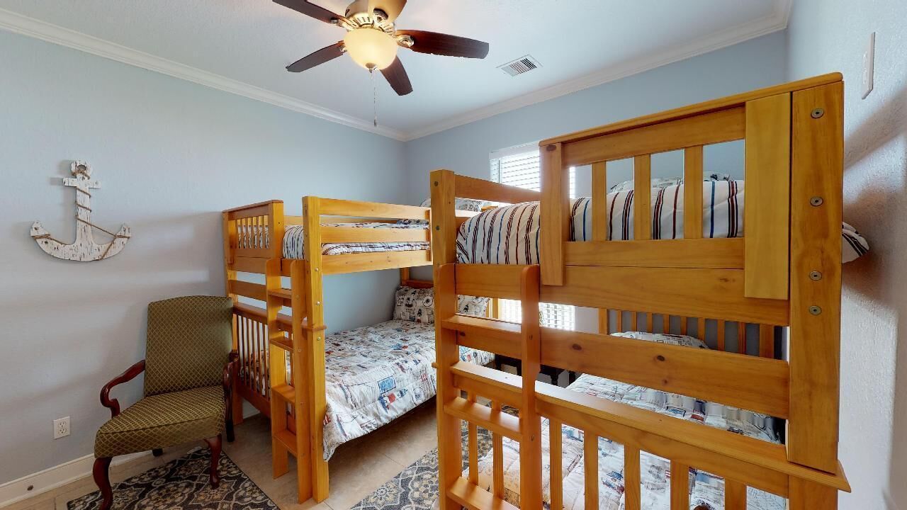 Ein Zimmer mit Etagenbetten, einem Sessel, einem Deckenventilator und einem gemusterten Teppich.