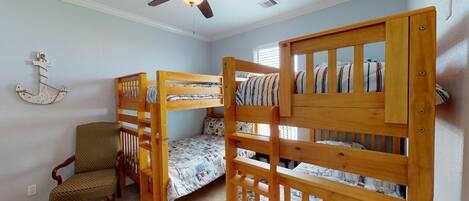 Ein Zimmer mit Etagenbetten, einem Sessel, einem Deckenventilator und einem gemusterten Teppich.