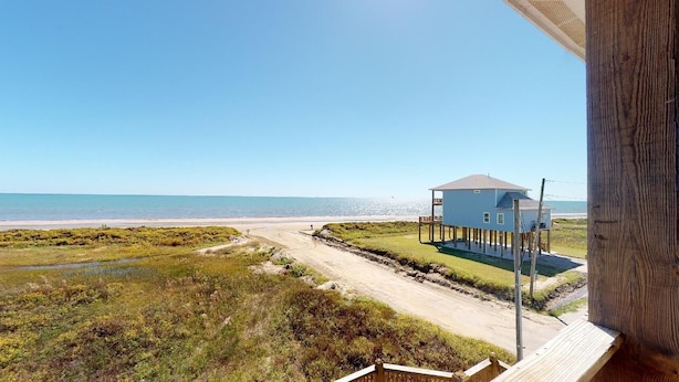 Vista costera con una casa sobre pilotes, una playa y cielo despejado.