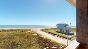 A coastal view with a house on stilts, a beach, and a clear sky.