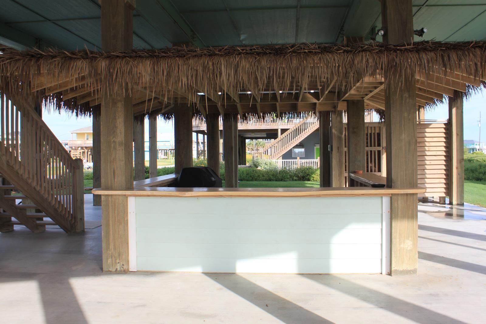 A covered outdoor area with a wooden bench, a thatched roof, and a concrete floor.