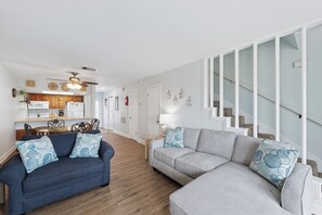 Ein Wohnzimmer mit einem blauen Sofa, einem grauen Ecksofa und einer Treppe mit weißen Geländern.