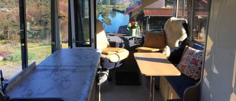 A camper van interior with a kitchen area, seating, and a view of a lake and hills.
