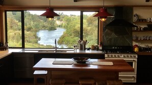 Een keuken met een groot raam met uitzicht op een rivier, houten balken, een fornuis en een gootsteen.