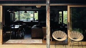 Een ruime eethoek met een grote tafel en stoelen, een keuken met uitzicht op de omgeving, en een houten paal in het midden.