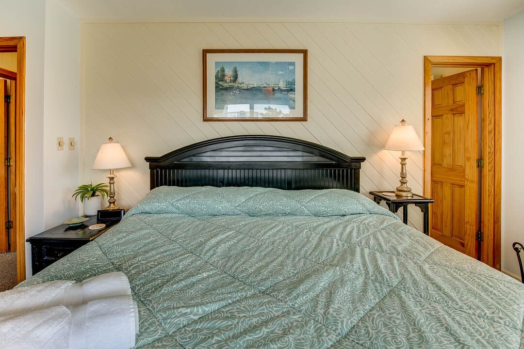 A neatly arranged bedroom with a bed, two bedside tables, a nightstand, a framed picture on the wall, and wooden doors.