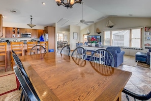 A spacious dining area with a wooden table and chairs, a kitchen with wooden cabinets, and a large window with blinds.