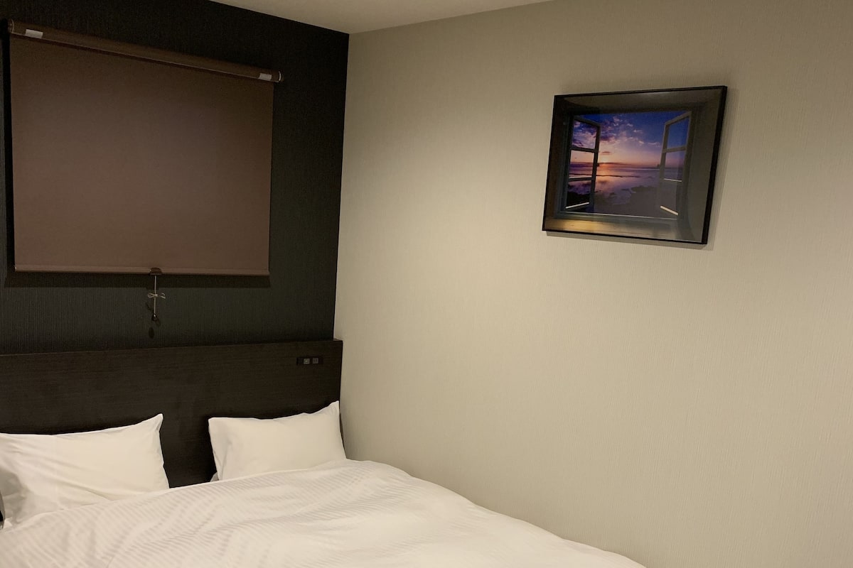 A hotel room with a large bed, a headboard, a window, and a framed picture on the wall.