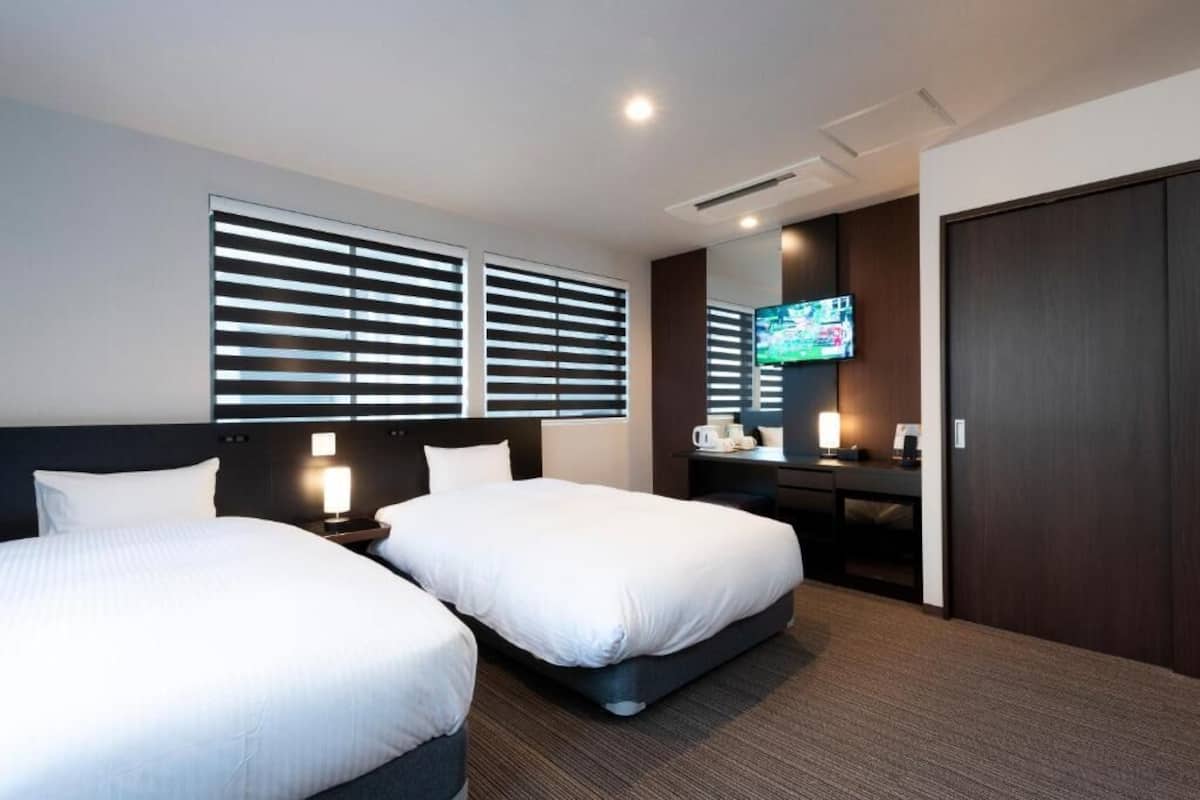 A hotel room with two beds, a TV, a desk, and a wardrobe.