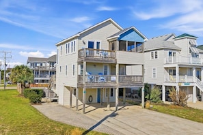 A multi-story residential building with a balcony on the second floor, a covered porch, and a garage.