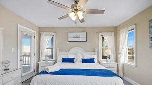 A bedroom with a bed, white curtains, a ceiling fan, and a window with a view. - Spur of the Moment | 293 ft from the beach | Private Pool, Hot Tub | Kill Devil Hills (Kill Devil Hills)