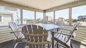 A covered patio with a table and chairs, large windows, and a view of the surrounding neighborhood. - Spur of the Moment | 293 ft from the beach | Private Pool, Hot Tub | Kill Devil Hills (Kill Devil Hills)