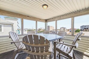 A covered patio with a table and chairs, large windows, and a view of the surrounding neighborhood. - Spur of the Moment | 293 ft from the beach | Private Pool, Hot Tub | Kill Devil Hills (Kill Devil Hills)