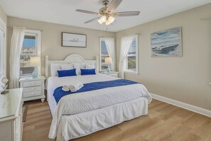Un dormitorio con cama, mesita de noche, ventilador de techo y ventana con cortinas.