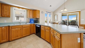 A kitchen with wooden cabinets, a dishwasher, and a large island with chairs. - Spur of the Moment | 293 ft from the beach | Private Pool, Hot Tub | Kill Devil Hills (Kill Devil Hills)