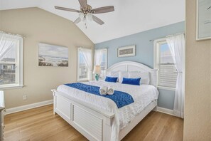 A bedroom with a bed, ceiling fan, and two windows with curtains.