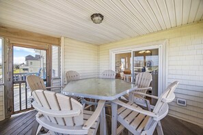 Un área de comedor al aire libre techada con una mesa de vidrio y sillas de madera, una terraza de madera y vistas al vecindario.