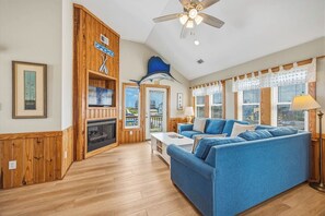 Una sala de estar amplia con chimenea, un sofá azul y un ventilador de techo.