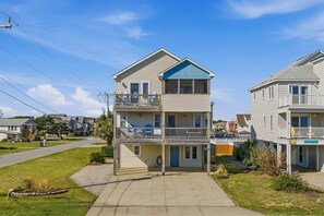 A two-story residential building with a front porch, a balcony on the upper floor, and a visible garage door. - Spur of the Moment | 293 ft from the beach | Private Pool, Hot Tub | Kill Devil Hills (Kill Devil Hills)