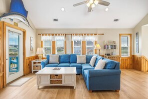 A living room with a blue sectional sofa, a white coffee table, and a ceiling fan.