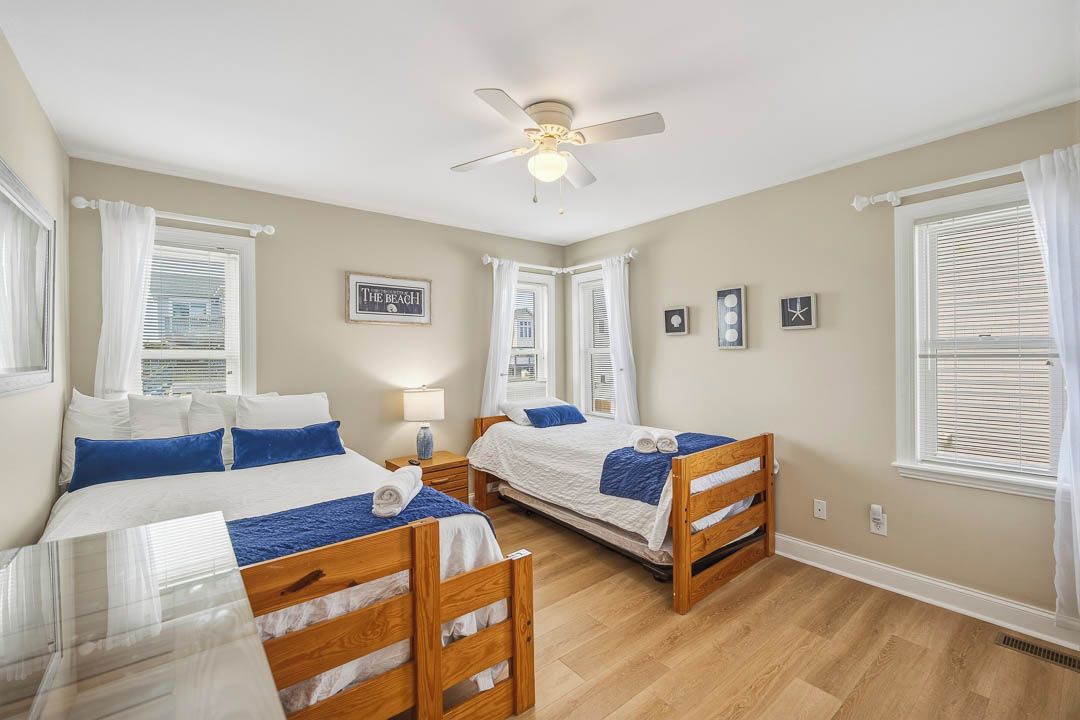 A bedroom with two wooden beds, a ceiling fan, and a window with white curtains.