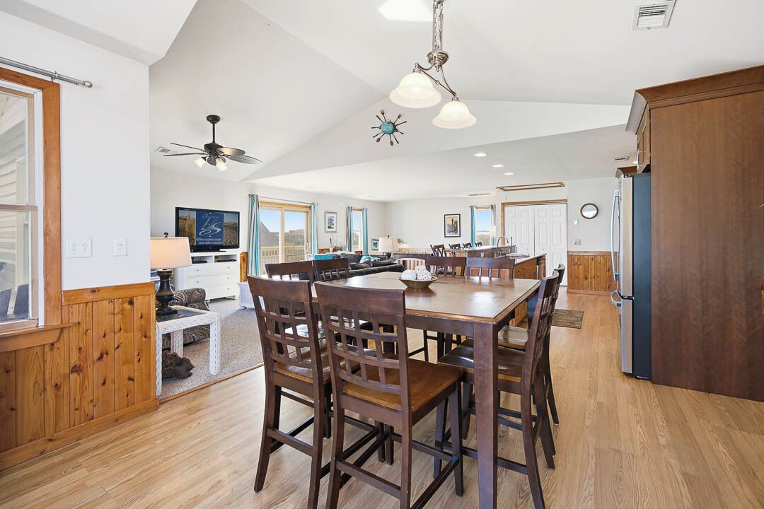 A spacious kitchen with wooden flooring, a central island, and modern lighting fixtures.