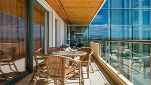 A balcony with wicker furniture and a glass table, overlooking a cityscape.