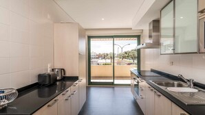Una cocina moderna con encimera negra, electrodomésticos de acero inoxidable y vistas al exterior a través de un ventanal.