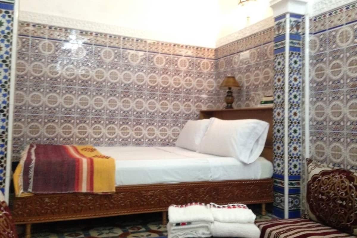 A room with a bed, a nightstand, a lamp, and patterned walls.